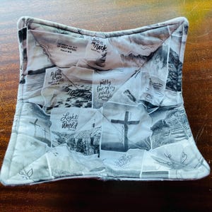 May include: A white quilted fabric bowl with a patchwork design featuring various inspirational quotes and images. The quotes include "Lord is my Rock", "Be Still", "Justly Love Mercy Walk Humbly", and "Light of the World".