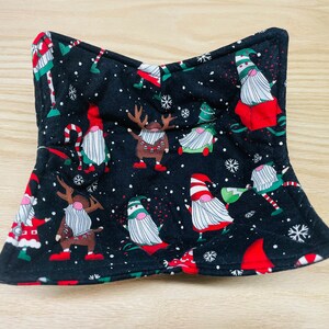 May include: Black fabric pot holder with a Christmas gnome pattern. The gnomes are wearing red hats and have white beards. There are also snowflakes and Christmas trees on the fabric.