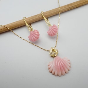 May include: A delicate gold chain necklace with a pink shell pendant accented with small clear stones. Matching pink shell earrings with gold hooks.