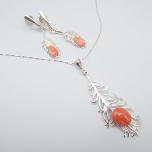 May include: A silver necklace and earrings set with a delicate feather design and a pink coral stone accent.