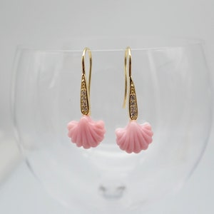 May include: A pair of gold earrings with a pink shell design and clear crystal accents.