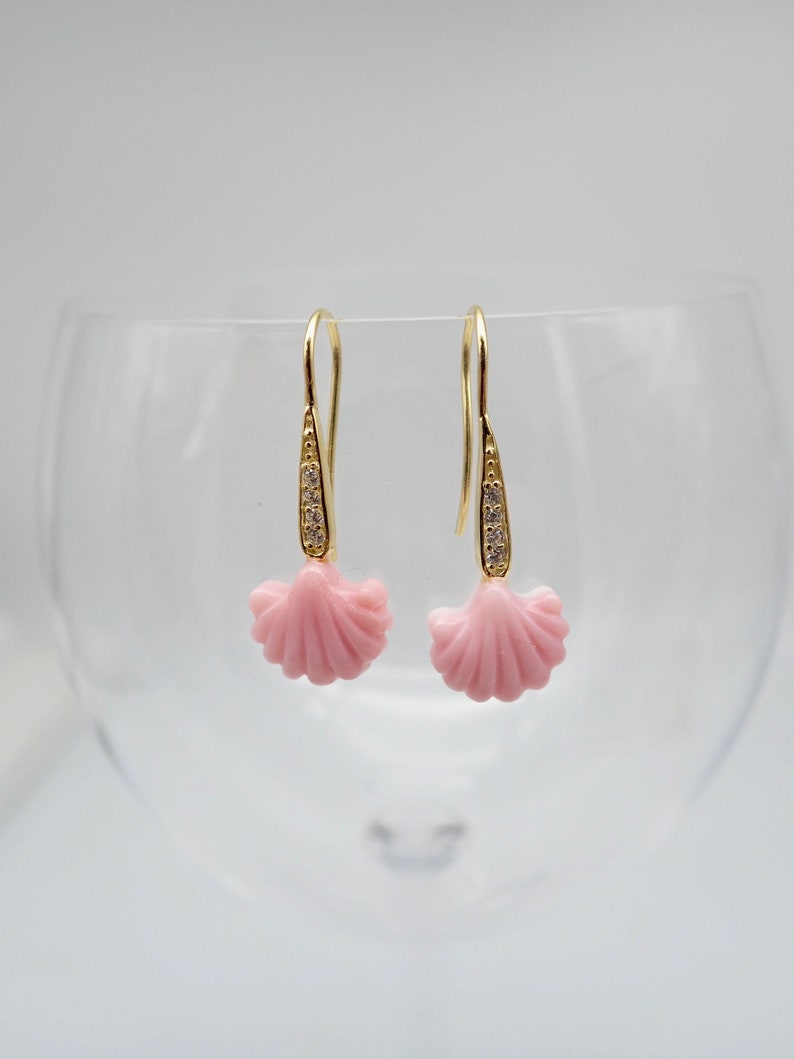 May include: A pair of gold earrings with a pink shell design and clear crystal accents.