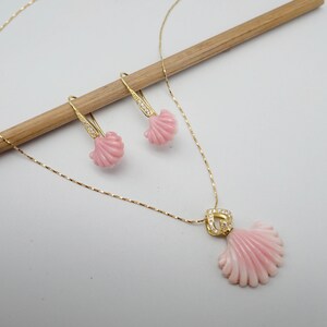 May include: A gold necklace and earrings set featuring pink shell pendants. The necklace has a delicate chain and the earrings have a drop design.