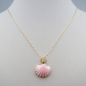 May include: A gold chain necklace with a pink shell pendant accented with clear rhinestones.