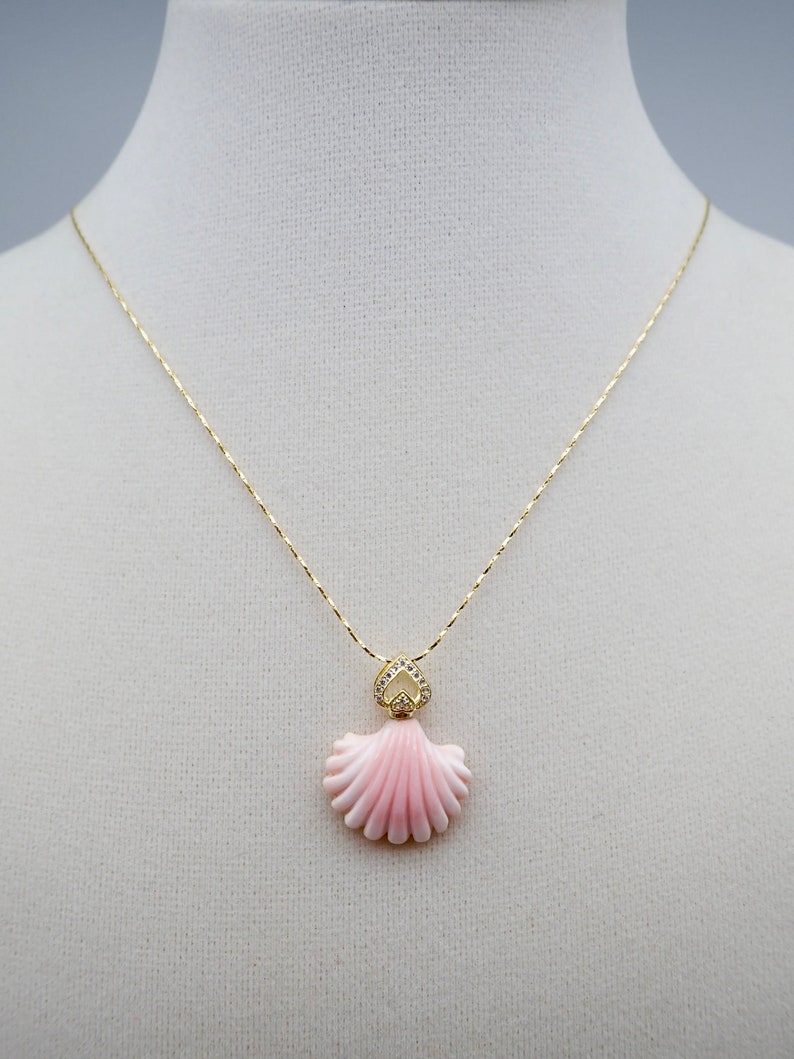 May include: A gold chain necklace with a pink shell pendant accented with clear rhinestones.