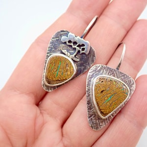 May include: A pair of silver earrings with a textured finish and a brown opal stone set in each. The earrings have a tree-shaped design on the top.