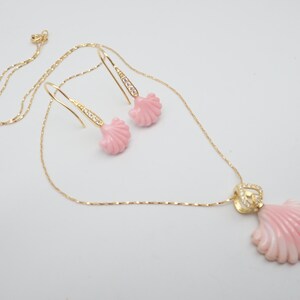 May include: A delicate gold chain necklace with a pink seashell pendant and matching earrings. The pendant and earrings are adorned with small clear crystals.
