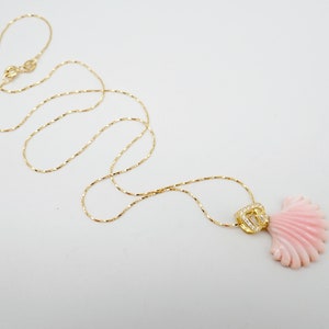 May include: A delicate gold chain necklace with a pink coral shell pendant. The pendant features a small gold charm with clear stones.