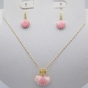 May include: A delicate gold necklace and earrings set featuring pink coral shell pendants with diamond accents. The necklace has a delicate chain and the earrings are drop style.