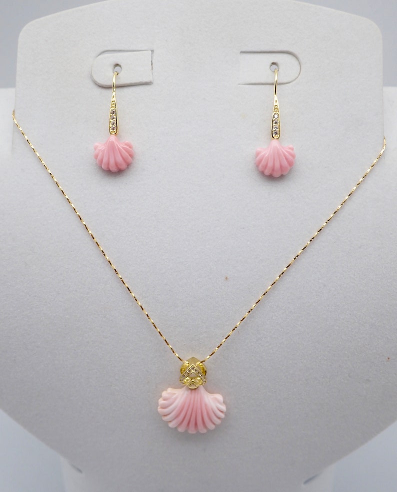 May include: A delicate gold necklace and earrings set featuring pink coral shell pendants with diamond accents. The necklace has a delicate chain and the earrings are drop style.