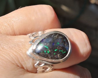 May include: A silver ring with a black opal gemstone. The opal has green and blue flashes of color.