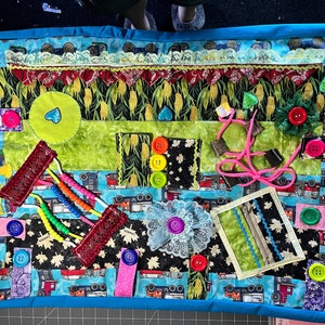 Puede incluir: Un libro silencioso de tela colorido con varias texturas y actividades para niños. Presenta una variedad de colores, incluyendo azul, verde, rojo y amarillo. El libro incluye una cremallera, botones, cuentas y otros elementos interactivos.