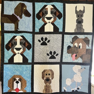 May include: A quilt with a patchwork design featuring various dog breeds, including a brown and white dog, a black and white dog, a brown dog, and a gray dog. The quilt also features paw prints and a light blue background.