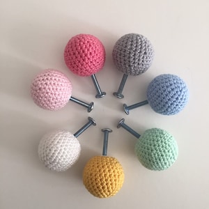 Può includere: Otto pomelli all'uncinetto in vari colori pastello, tra cui rosa, azzurro, giallo, verde e bianco, con viti argentate.