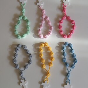 May include: Six crocheted rosaries with wooden crosses. The rosaries are in different colors: green, pink, red, gray, yellow, and blue.