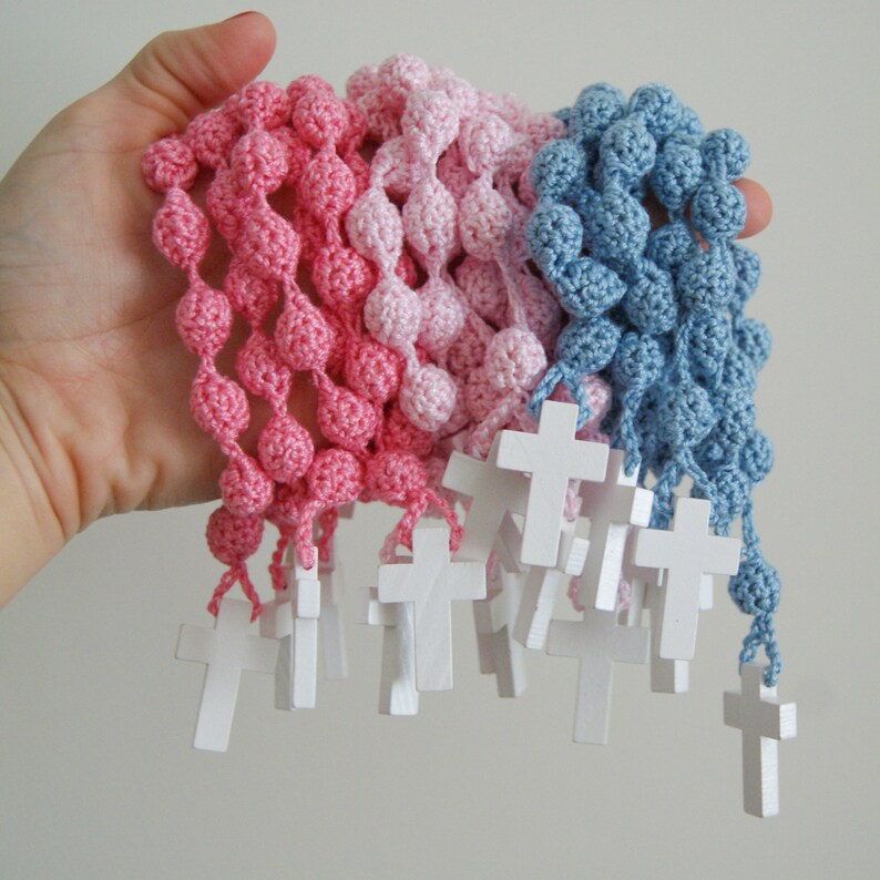 May include: A set of crocheted rosaries with wooden cross charms. The rosaries are pink, light pink, and blue.