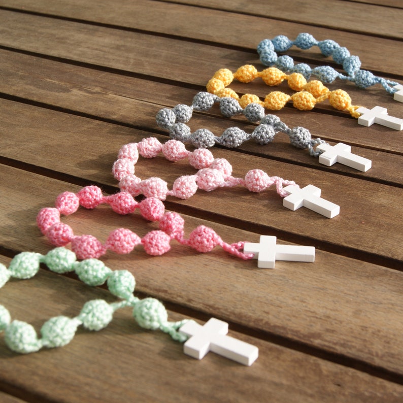 May include: Five crocheted rosaries with wooden crosses. The rosaries are in shades of green, pink, gray, yellow, and blue.