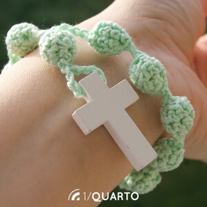 May include: A green crocheted bracelet with a white wooden cross charm. The bracelet is made with small, round beads and has a simple design.