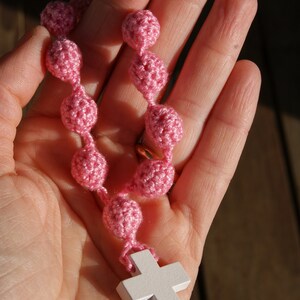 May include: A pink crocheted rosary with a white wooden cross.