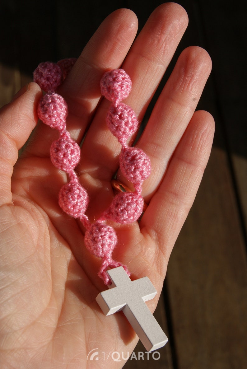May include: A pink crocheted rosary with a white wooden cross.