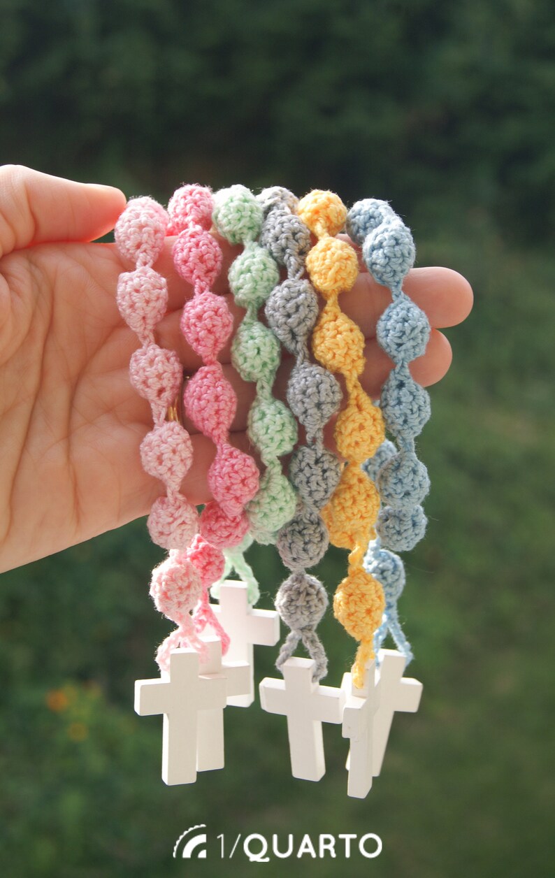 May include: A set of seven crocheted beaded necklaces with wooden cross charms. The necklaces are in pastel colors: pink, light blue, green, gray, and yellow.