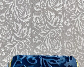 May include: A blue paint roller with a decorative pattern of swirling leaves and flowers. The roller is made of a durable material and is designed to create a unique and elegant look on walls.