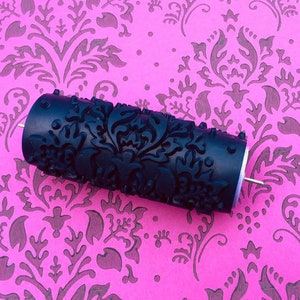 May include: A black paint roller with a damask pattern. The roller is on a pink background with a damask pattern.