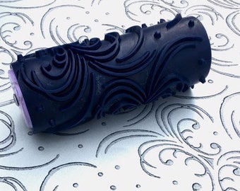 以下が含まれることがあります： 渦巻きと点の装飾的なパターンが施された黒いペイントローラー。ローラーは、ローラーによって作成された一致するパターンを持つ白い表面上にあります。