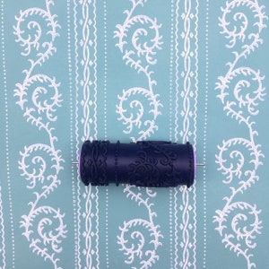 Puede incluir: Un rodillo de pintura con estampado negro y morado con un pasador de metal. El rodillo está sobre un fondo estampado azul y blanco.