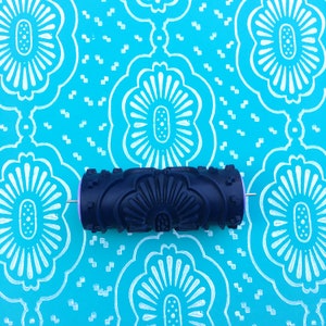 May include: A blue and black patterned paint roller with a white handle. The roller is on a blue background with a white floral pattern.