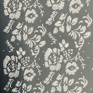 Puede incluir: Un fondo gris con un patrón floral blanco. El patrón está formado por flores y hojas estilizadas.