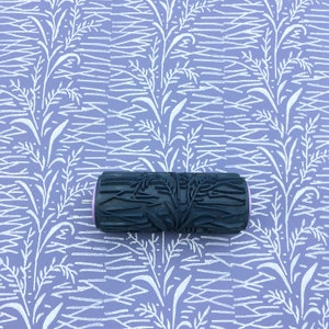 Op de afbeelding: Een zwart-witte verfroller met een bloemenpatroon. De roller bevindt zich op een paarse achtergrond met een wit bloemenpatroon.