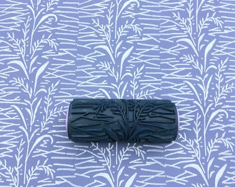 May include: A black and white paint roller with a floral design. The roller is on a purple background with a white floral pattern.
