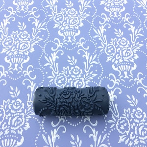 Könnte beinhalten: Eine schwarze und silberne Farbrolle mit einem Blumenmuster. Die Rolle befindet sich auf einem violetten Hintergrund mit einem weißen Blumenmuster.