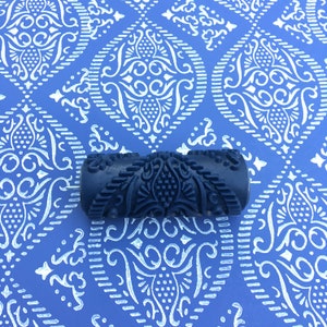 May include: A black paint roller with a decorative pattern. The roller is designed to create a damask pattern on walls or other surfaces.