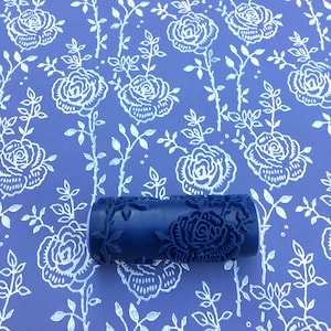 May include: A blue paint roller with a floral design. The roller is on a blue background with a white floral pattern.