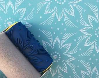 May include: A blue and yellow paint roller with a floral design. The roller is on a light blue background with a white floral pattern.