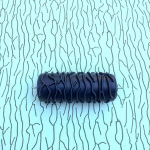 Può includere: Un rullo di vernice nero con un designo testurizzato che ricorda la corteccia di un albero. Il rullo è su uno sfondo blu chiaro con un motivo simile.