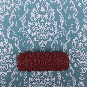 May include: A red paint roller with a damask pattern. The roller is designed to create a decorative pattern on walls.