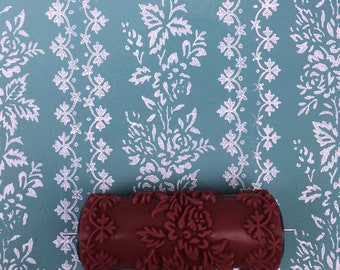 May include: A red paint roller with a floral design. The roller is on a blue background with a white floral pattern.