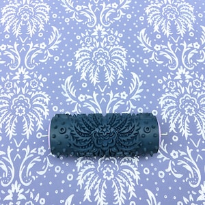 May include: A black paint roller with a detailed floral pattern. The roller is on a purple background with a white floral pattern.