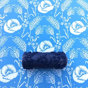 May include: A blue paint roller with a floral design. The roller is on a blue background with a white floral pattern.