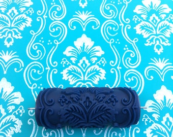 May include: A blue paint roller with a damask pattern. The roller is on a blue background with a white damask pattern.