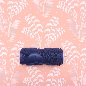 May include: A blue paint roller with a fern pattern. The roller is on a pink background with a white fern pattern.