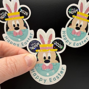 May include: Holographic stickers featuring Mickey Mouse dressed for Easter, wearing bunny ears and a yellow hat. The stickers have the text "Happy Easter" and "2026". The Disney Treasure logo is also visible.