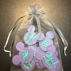 May include: A collection of purple Mickey Mouse-shaped charms with teal accents, displayed in a sheer, silver-tied bag. The charms feature various designs and the word "LOVE".