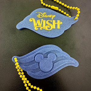 May include: Two blue, wing-shaped keychains with yellow ball chains. One keychain has the text "Disney WISH" in yellow. The other keychain features a Mickey Mouse head in the center. Both have yellow clasps.