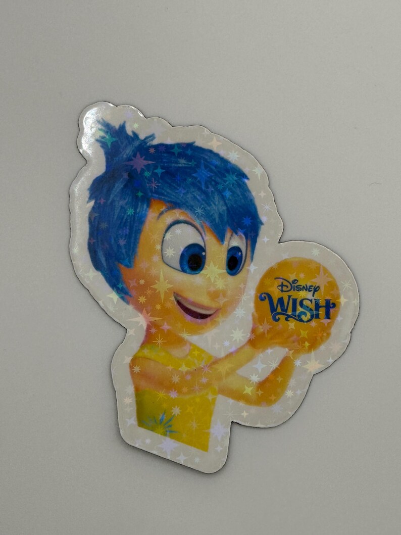 May include: A holographic sticker featuring the character Joy from Disney's "Inside Out" holding a golden orb with the "Disney Wish" logo. Joy has blue hair and a yellow dress, with a smiling expression.
