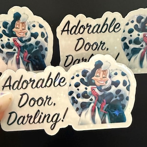 May include: A collection of stickers featuring a cartoon illustration of a woman with black and white hair and a black and white spotted coat. The stickers have the text "Adorable Door, Darling!" in black script.