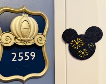 May include: A gold-colored Cinderella carriage emblem and a navy blue room number sign with the number 2559. A black Mickey Mouse head with yellow fireworks is on the right.